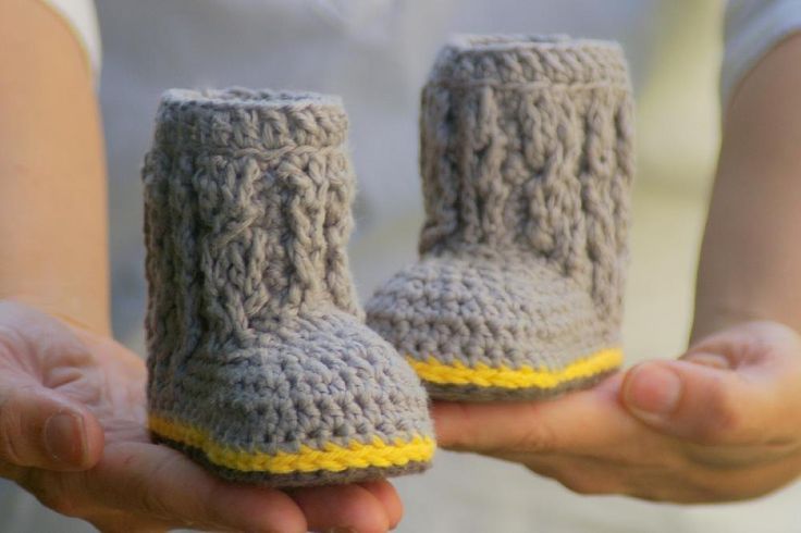 someone is holding two crocheted baby booties in their hands, one has a yellow strip on the bottom