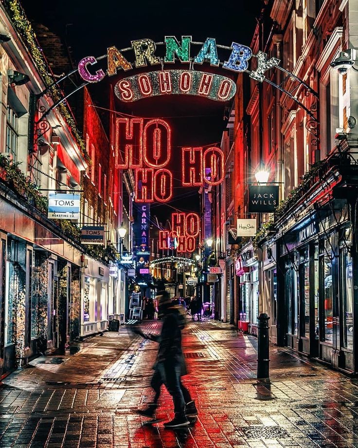 a person walking down a street at night with neon signs on the buildings behind them