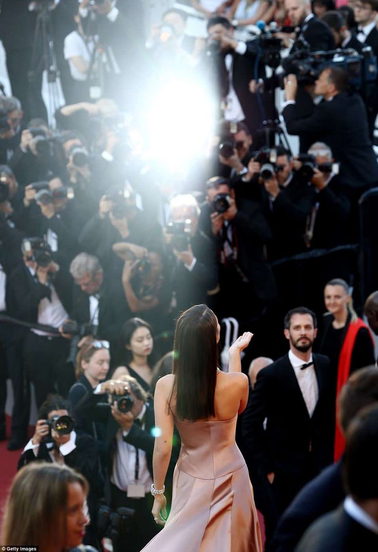 the back of a woman's dress as she walks down a red carpet in front of photographers