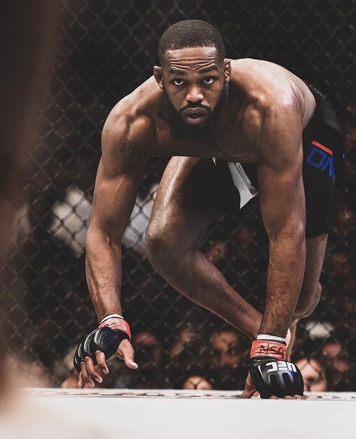 a man squatting down in front of a chain link fence with his hands on the ground