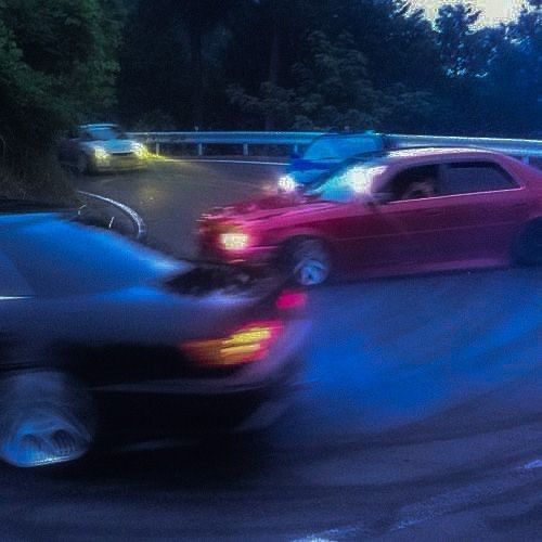 two cars driving down the road in front of each other at night with lights on