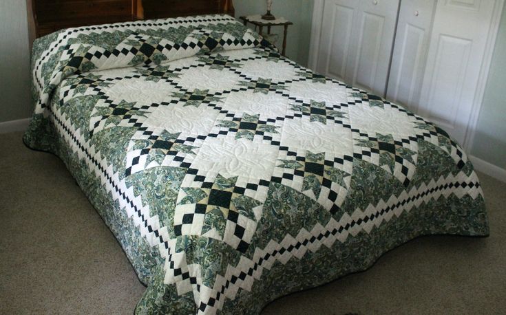 a bed with a green and white quilt on top of it next to a night stand