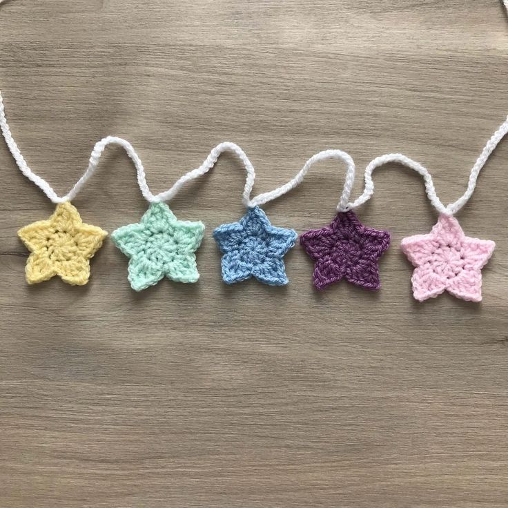 four crocheted stars are hanging from strings on a wooden surface, one is multicolored and the other has white string