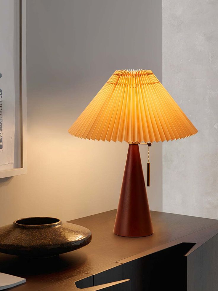 a table lamp sitting on top of a wooden desk next to a bowl and vase