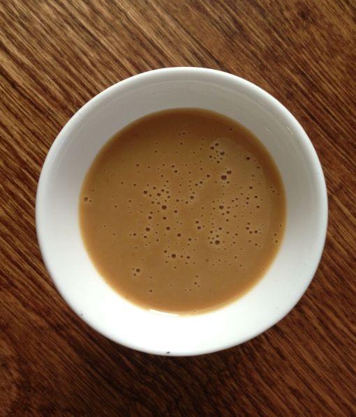 a white bowl filled with liquid on top of a wooden table next to a cup of coffee