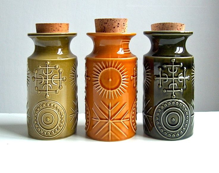 three ceramic vases are lined up in a row on a white surface, one has a corked top and the other is decorated with decorative designs