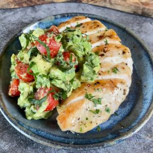 chicken with avocado and tomato salad on a blue plate