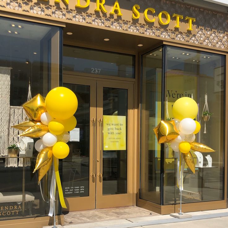 two large yellow and white balloons are in front of a storefront with the doors open