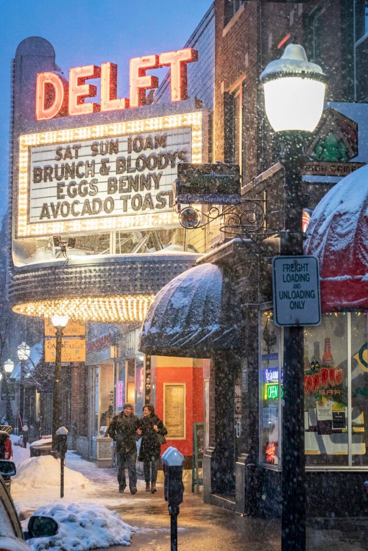 people are walking down the street in front of a movie theater on a snowy day