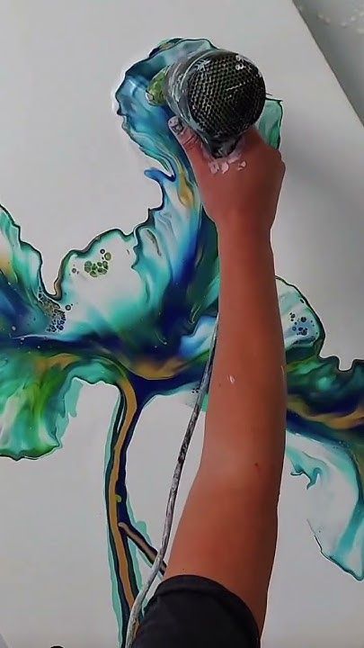 a person is using a brush to paint a flower on a white wall with blue, green and yellow swirls