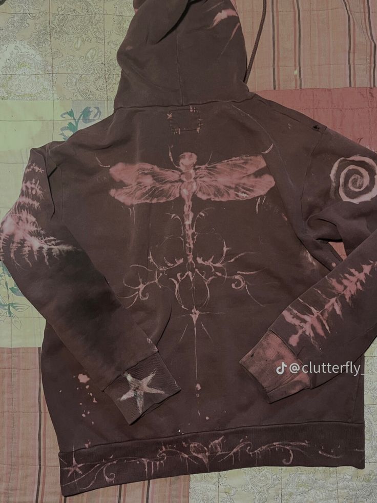 a brown hoodie with a dragon design on the front and back, sitting on a quilted surface