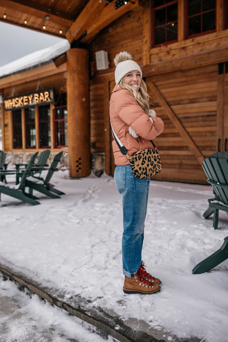 a woman standing in the snow with her hand on her hip and smiling at the camera