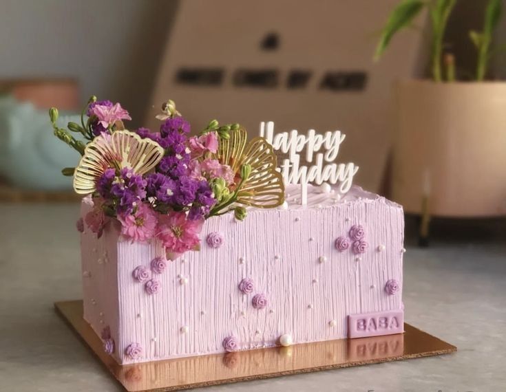 a pink birthday cake with flowers on it and a happy birthday sign in the middle