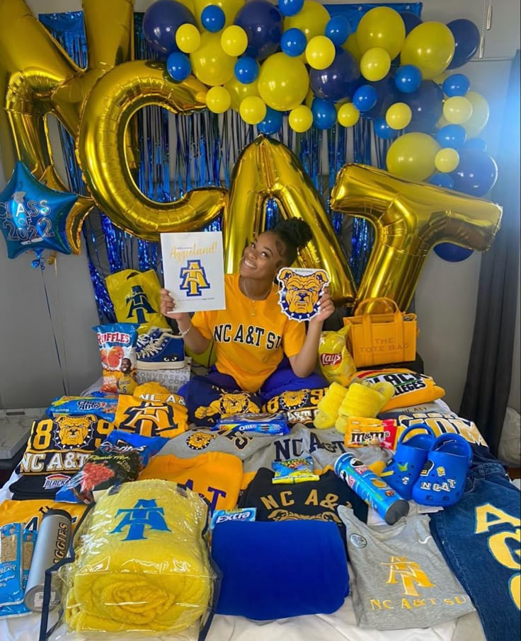 a woman sitting in front of a table with balloons and decorations on it, holding up a sign