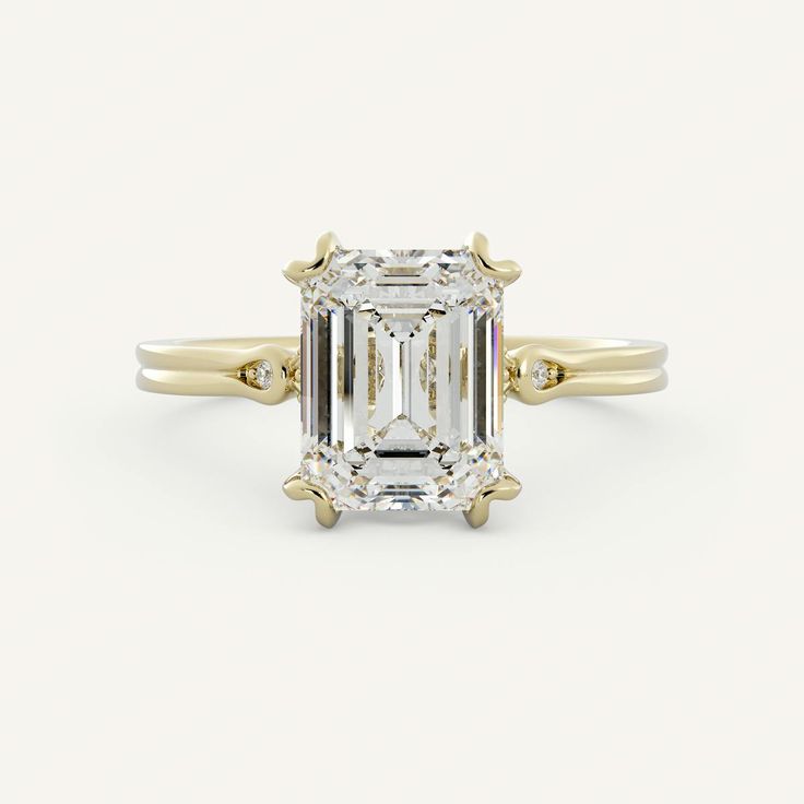 an emerald - cut diamond ring with two yellow gold band around the band, set against a white background