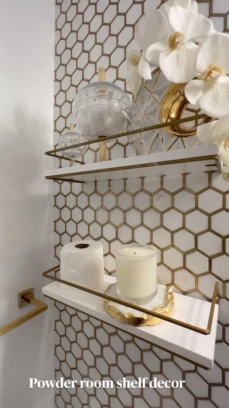 a bathroom with gold and white decor on the wall, toilet paper holder and shelf