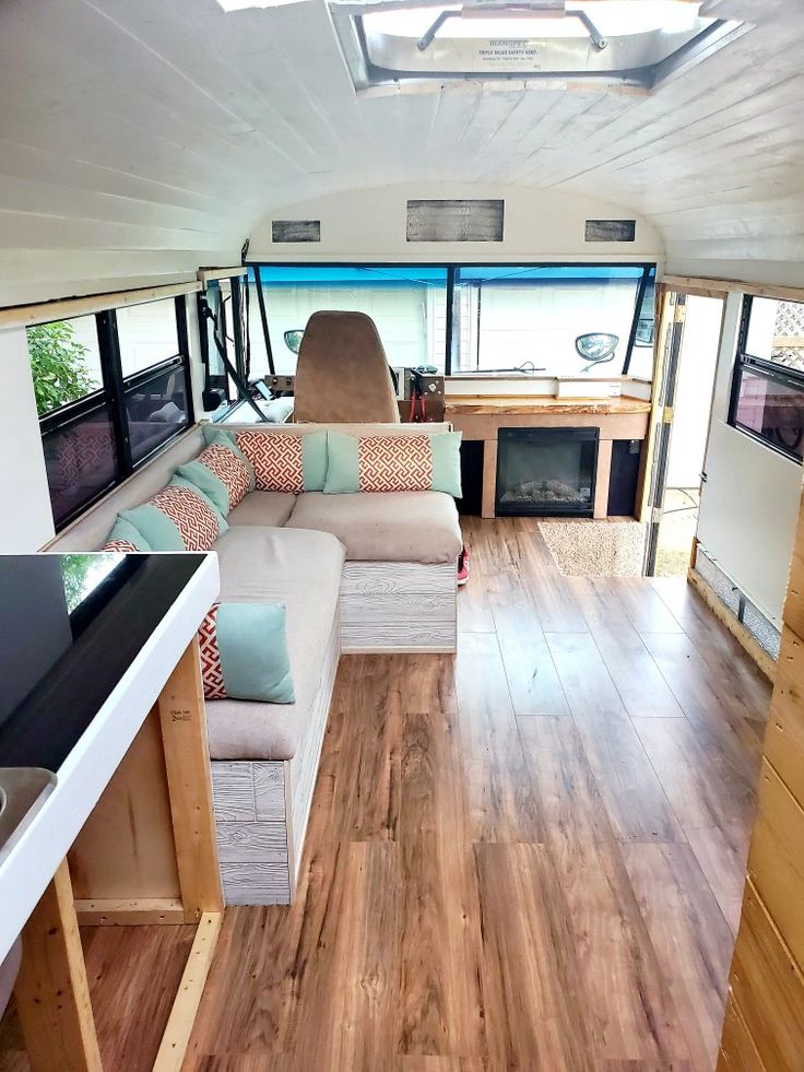 the interior of a camper with wood flooring and white couches, windows, and televisions