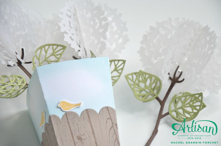 a paper bird sitting on top of a piece of wood next to some white flowers