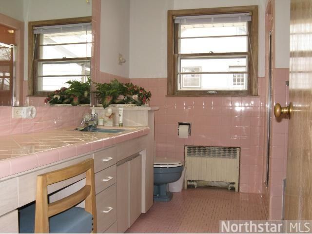 a bathroom with pink walls and tile flooring next to a sink, toilet and window