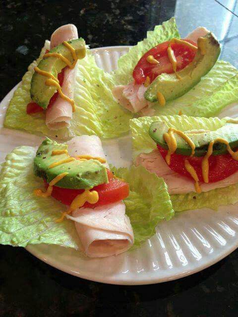 four lettuce wrapped sandwiches with tomatoes and avocado on a white plate