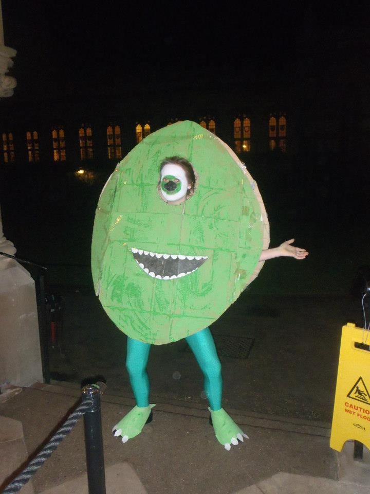 a man in a green costume standing next to a yellow sign with an evil face on it