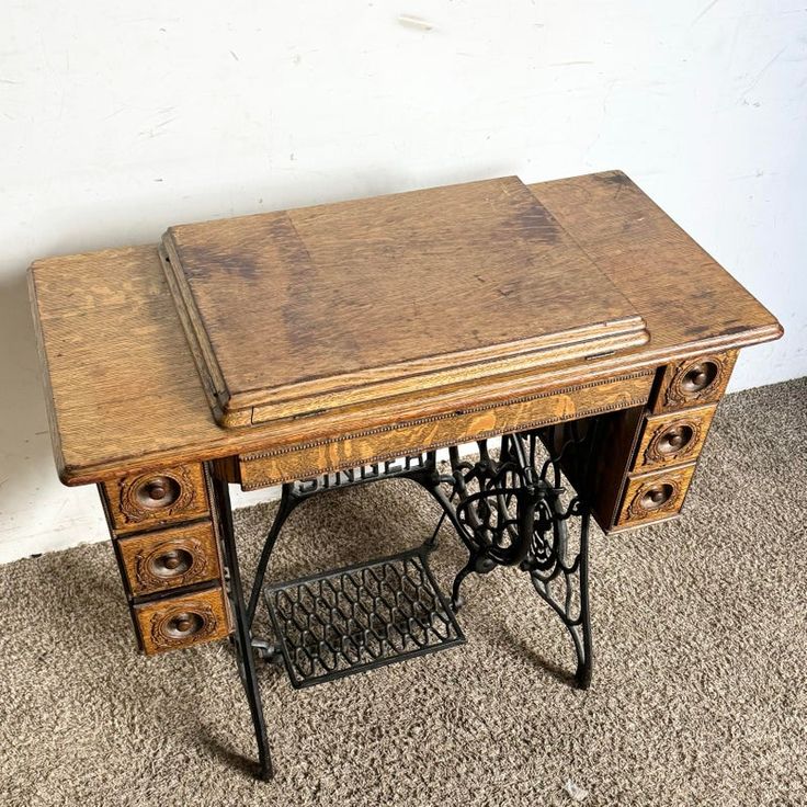 an old sewing machine sits on the floor next to a table with two drawers and a shelf