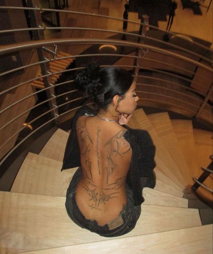 a woman with tattoos sitting on top of a wooden stair case while looking down at the floor