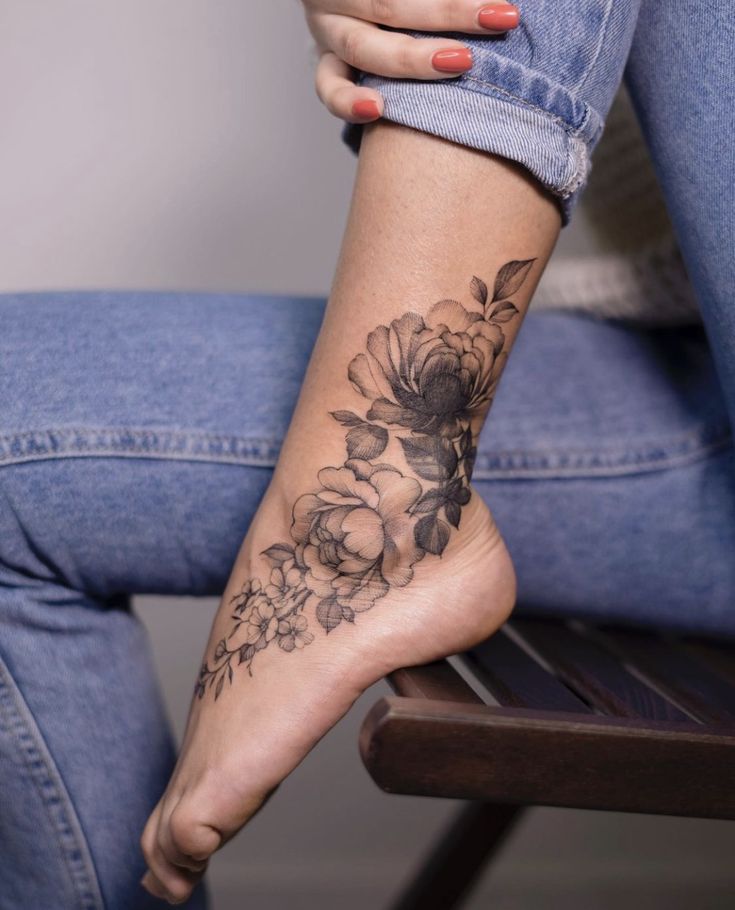 a woman's foot with a flower tattoo on her left leg, sitting on a chair