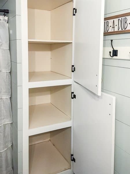 an open white cabinet in a bathroom next to a towel rack and toilet paper roll