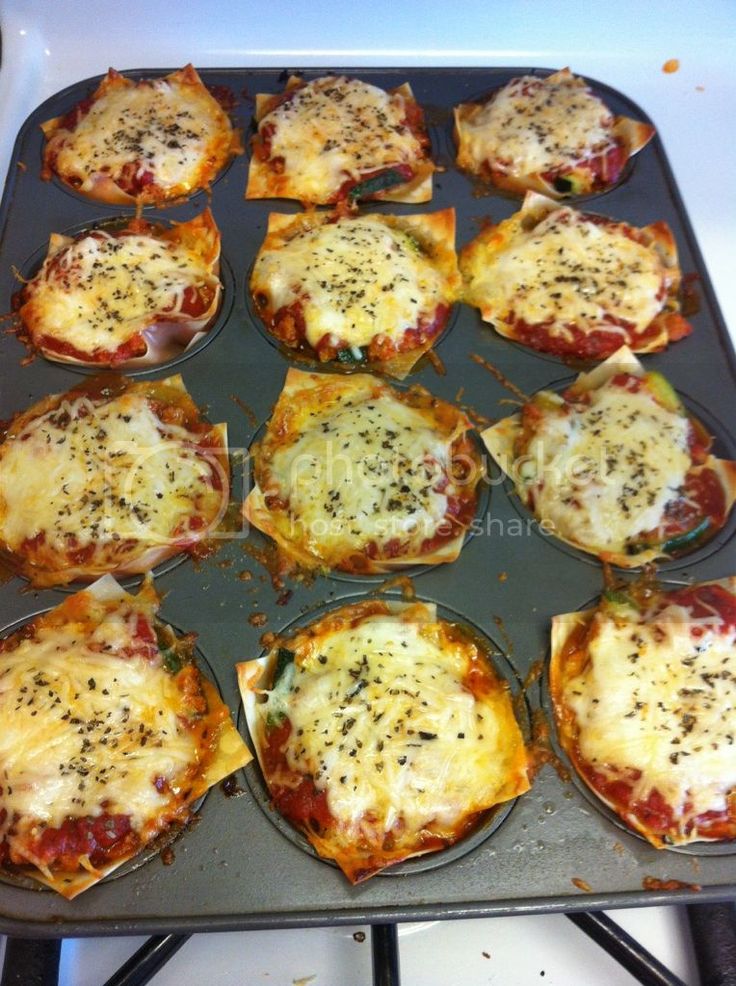 several mini pizzas are sitting in a muffin tin on top of the stove