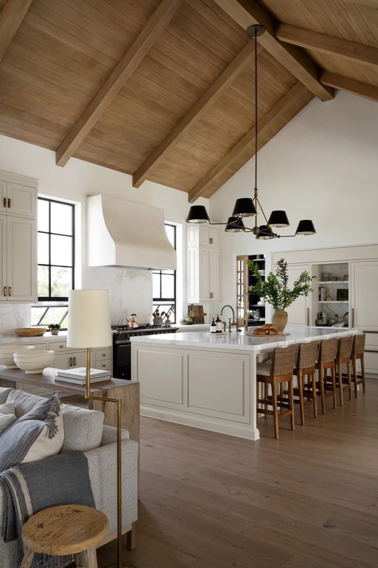 a large open kitchen and living room area with wood ceilinging, white walls, and wooden beams