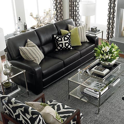 a living room with black leather couches and pillows on the coffee table in front of it