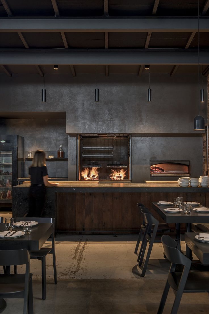 a woman is standing in front of an oven at a restaurant with tables and chairs