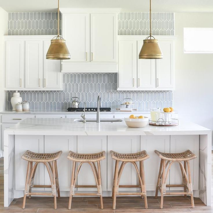 three stools sit at the center of a kitchen island with white cabinets and gold pendant lights