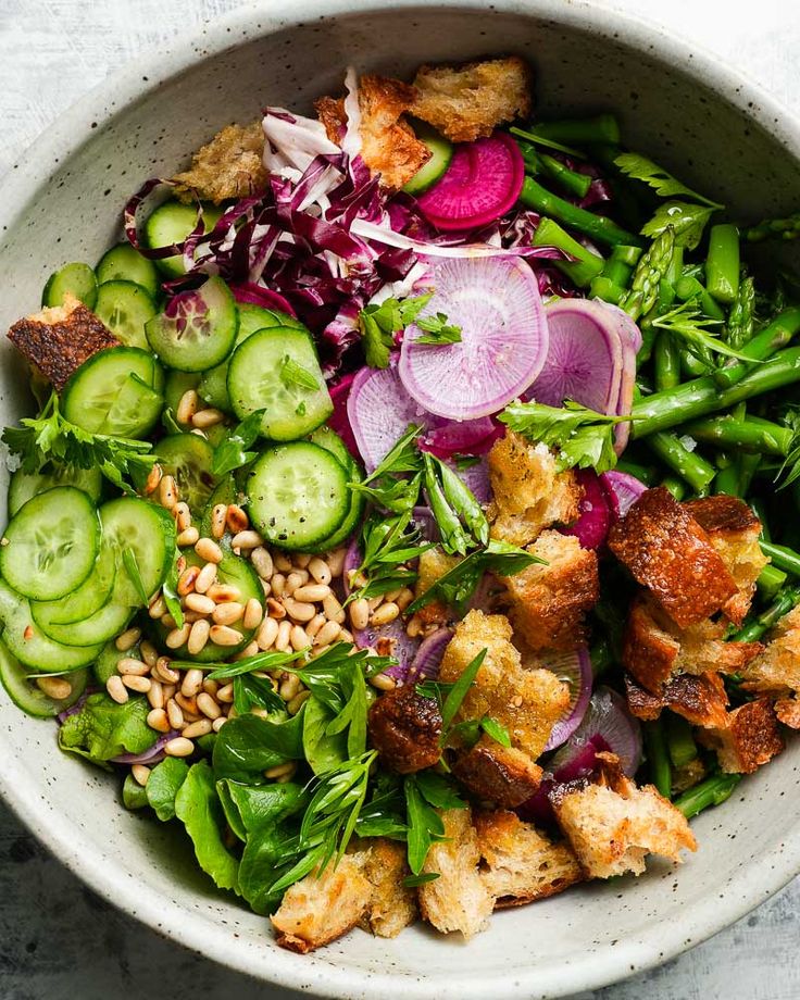 a white bowl filled with vegetables and meat on top of a marble countertop next to sliced cucumbers