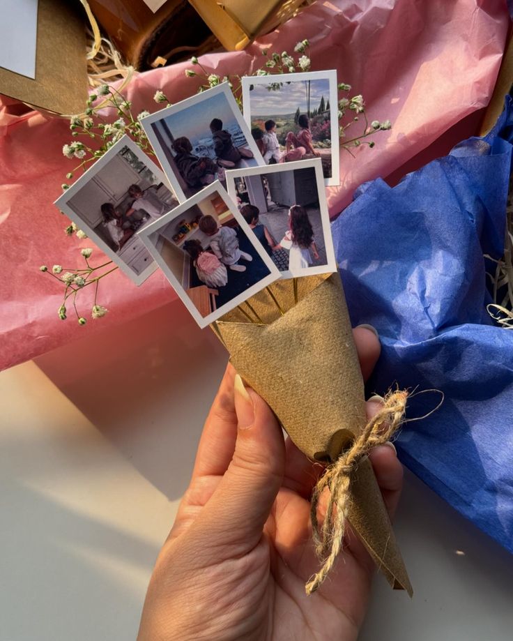 a person holding some pictures in their hand with flowers and ribbons around them on the table