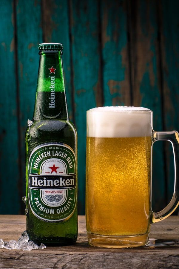 a beer bottle next to a glass full of beer on a wooden table with ice