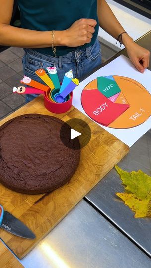 a woman standing in front of a chocolate cake on top of a wooden cutting board