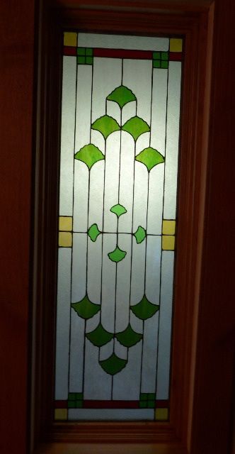 a stained glass door with green and yellow designs on the front panel, in a dark room