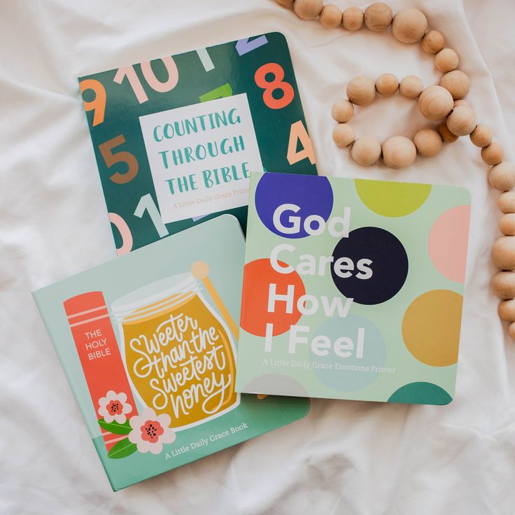 three children's books on a bed next to a bead necklace and wooden beads