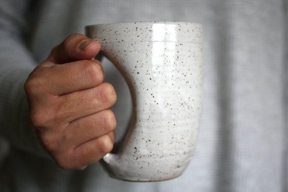 a person holding a white coffee cup in their left hand with speckles on it