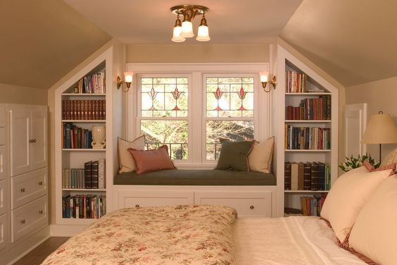 a bed sitting under a window in a bedroom next to a book shelf filled with books