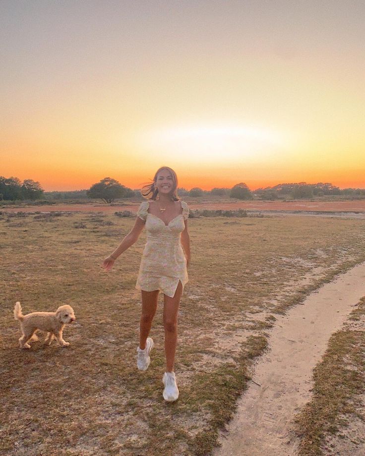 a woman is walking her dog in the middle of a grassy field at sunset or dawn