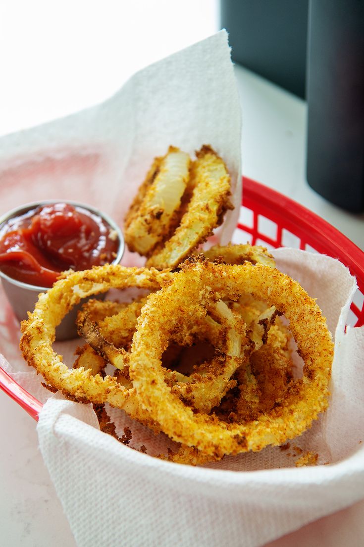 onion rings with ketchup and mustard in a red basket on a white table