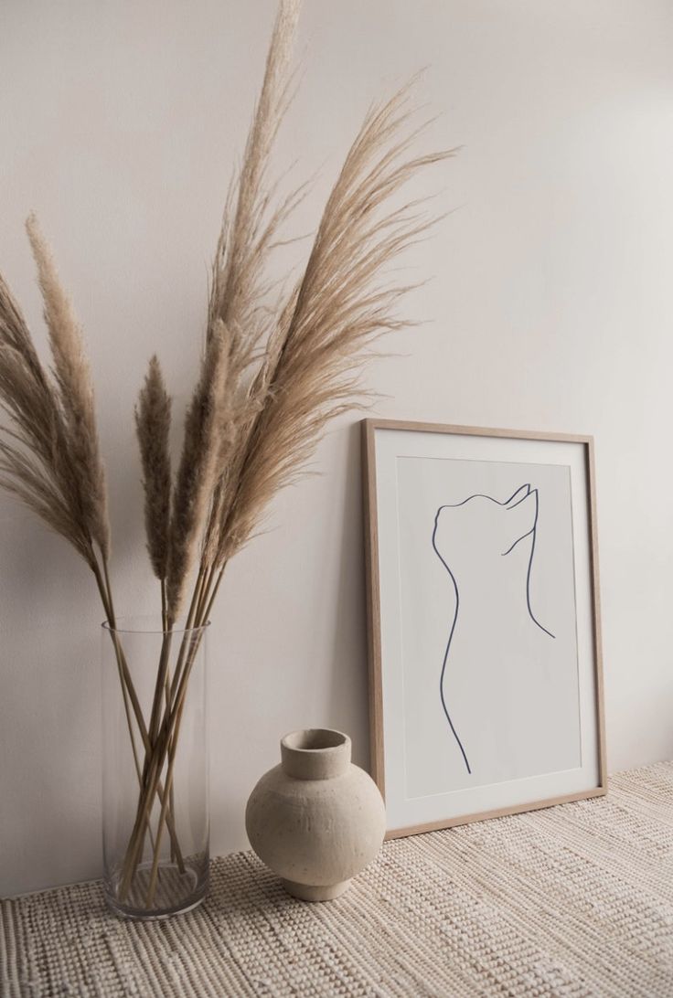 two vases with dry grass in them next to a framed photograph and art work