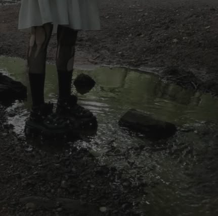 a woman standing on top of a puddle next to a forest