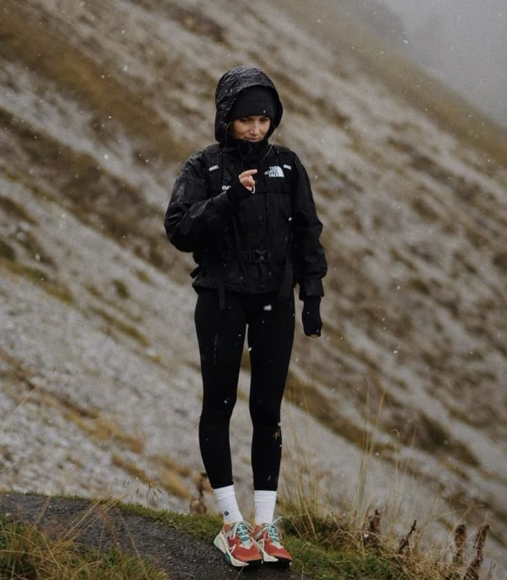 a woman standing on the side of a snow covered mountain with her hands in her pockets