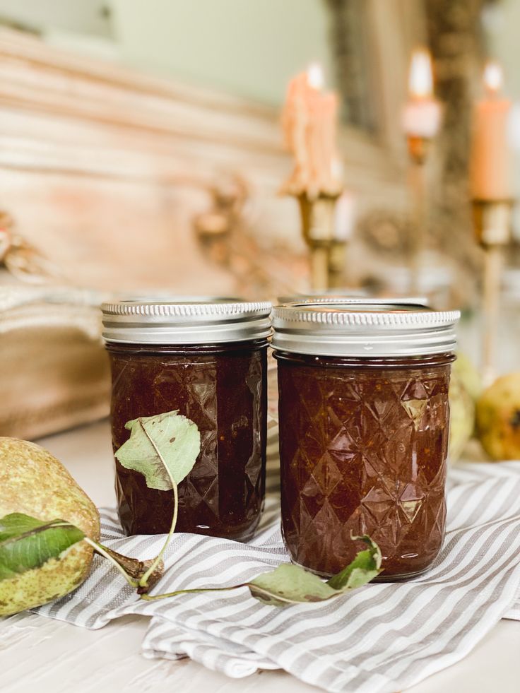 two jars filled with jam sitting on top of a table next to candles and fruit