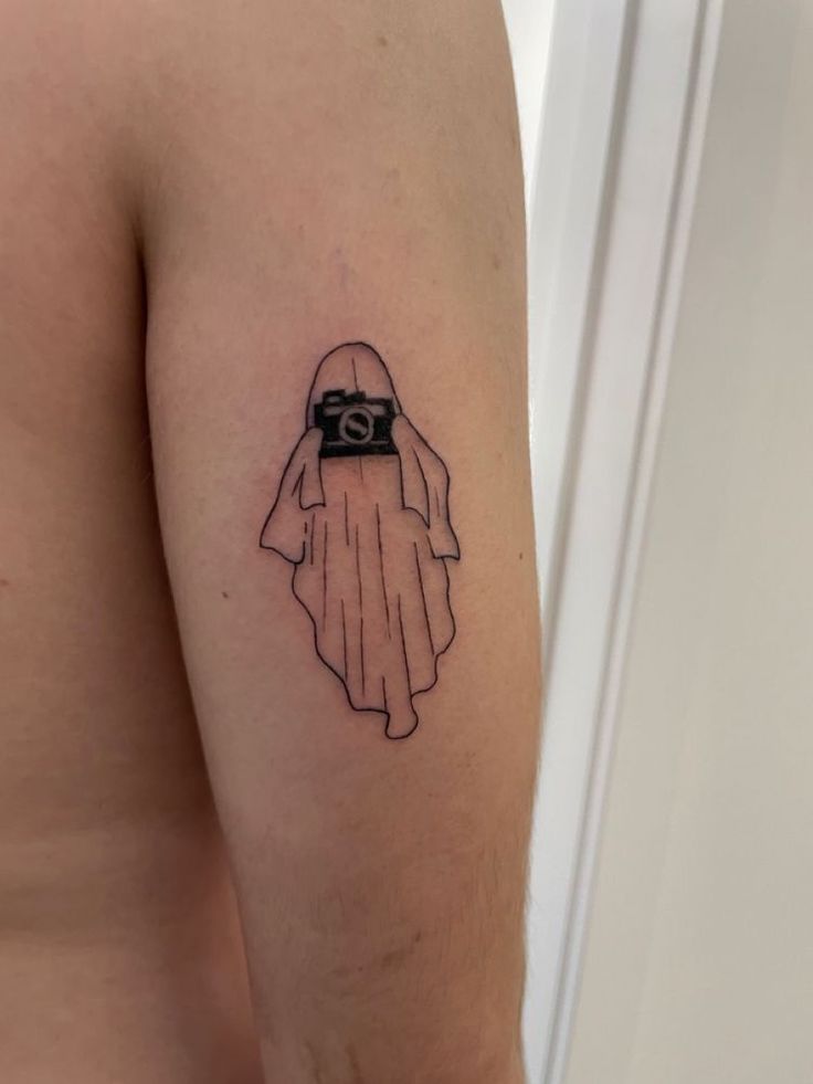 a person with a camera tattoo on their left arm and the image of a ghost behind them