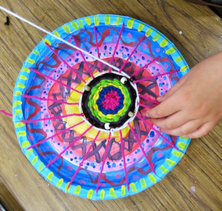 a person holding a colorful paper plate on top of a wooden table next to scissors